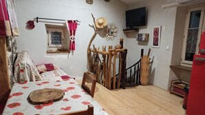 Un comedor con una mesa y sillas de madera, un adorno rústico en la pared, una ventana pequeña con cortinas y un televisor montado.