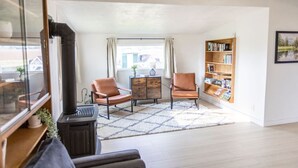 Un salón con chimenea, dos sillones de cuero, una estantería y un amplio ventanal con cortinas.