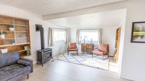 Amplia sala de estar con un sofá, dos sillones, una mesita, una chimenea y un ventanal grande.