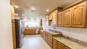 Una cocina amplia con armarios de madera, encimeras de granito y un refrigerador de acero inoxidable.