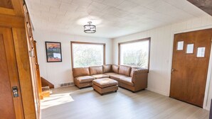 Un amplio salón con un sofá modular grande en forma de L, un pequeño reposapiés e iluminación en el techo.