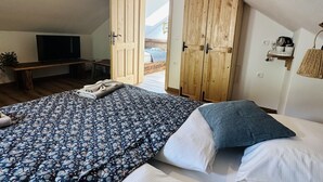 Un dormitorio con una cama grande, televisión, armarios de madera y una mesita con una planta.