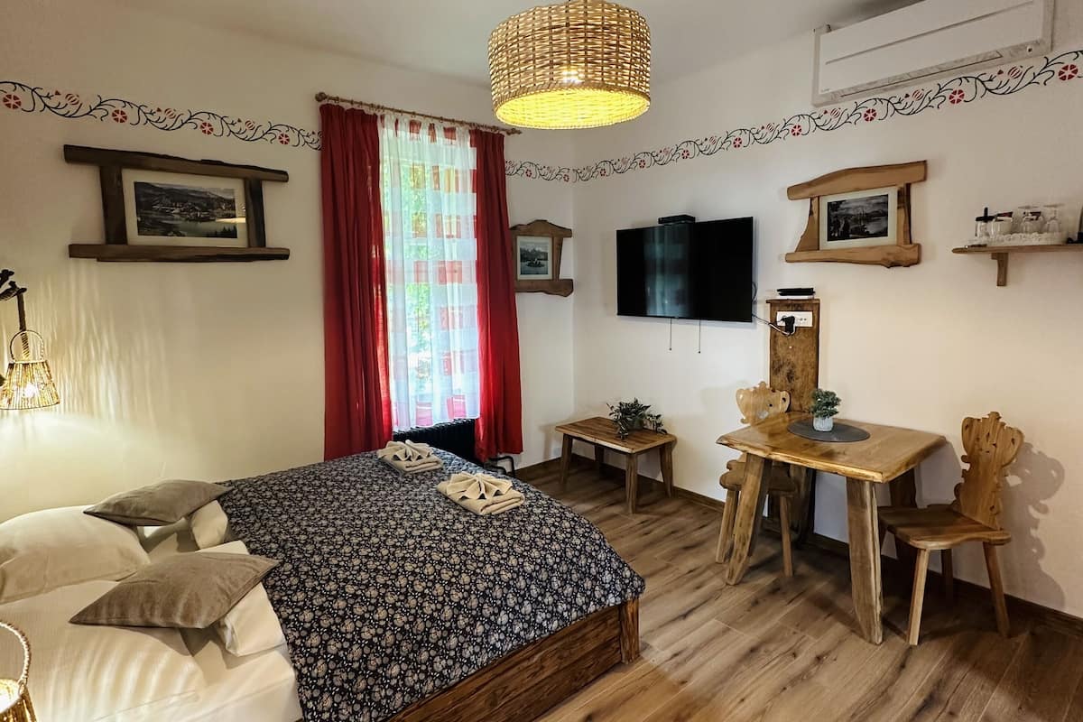 A bedroom with a bed, bedside tables, a desk, chairs, a TV, and a window with curtains.