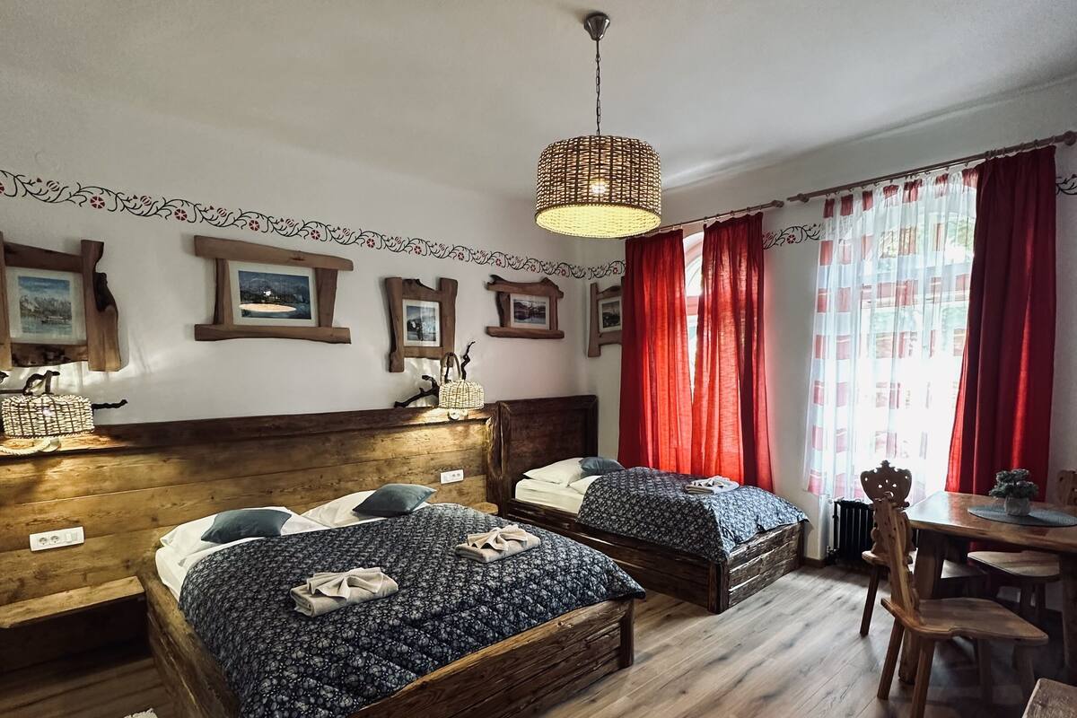 A cozy room with two wooden beds, a wooden dining table, and a hanging light fixture.