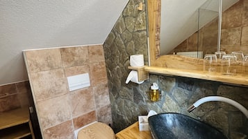 Ein Badezimmer mit einer Steinwand, einem Holzbadezimmermöbel, einem großen Waschbecken, einer Toilette und einem Spiegel mit Beleuchtung.