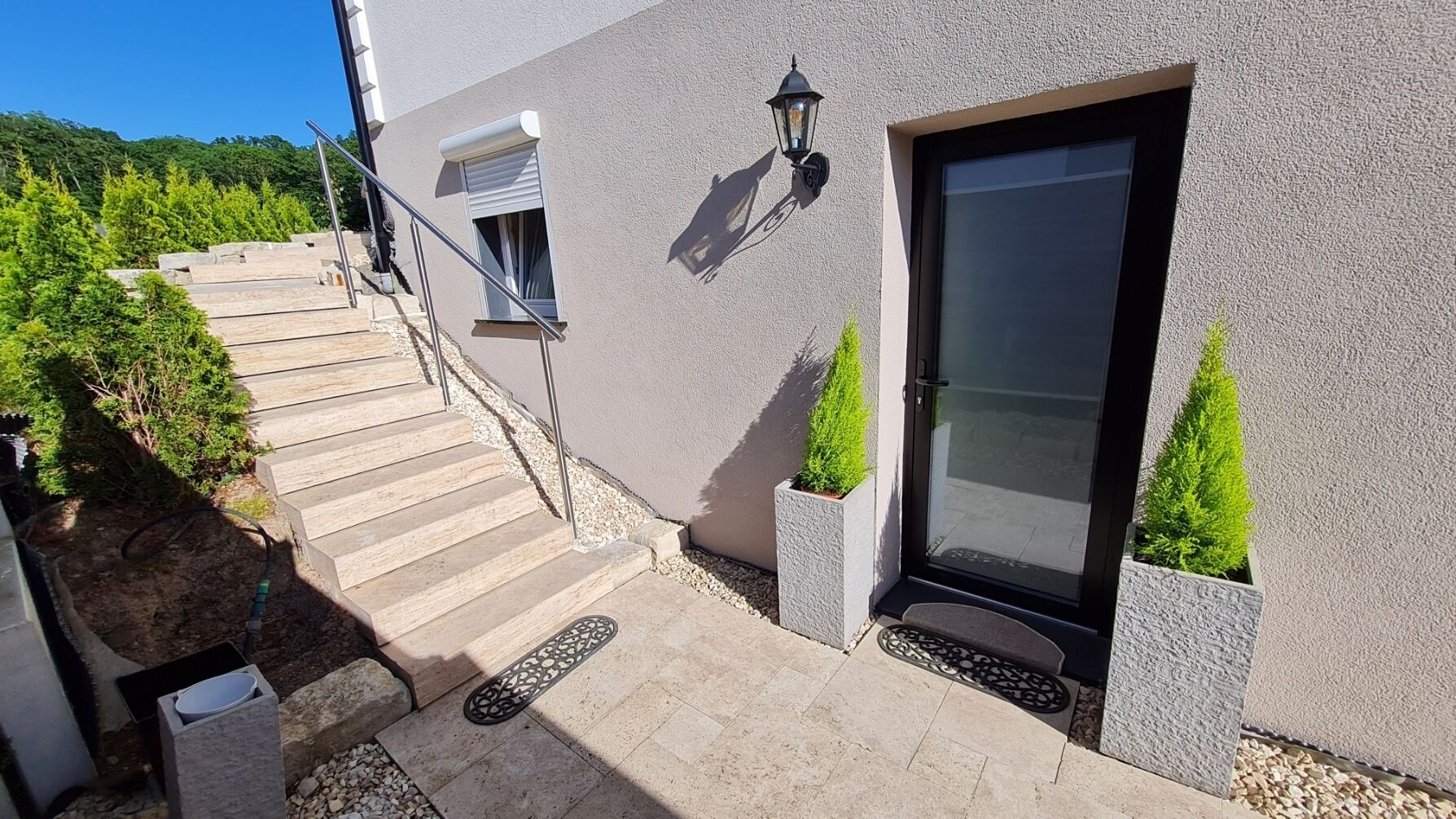 Ein modernes Gebäude mit einer Treppe, die zu einer Tür, einem kleinen Fenster und einer Wandleuchte führt.
