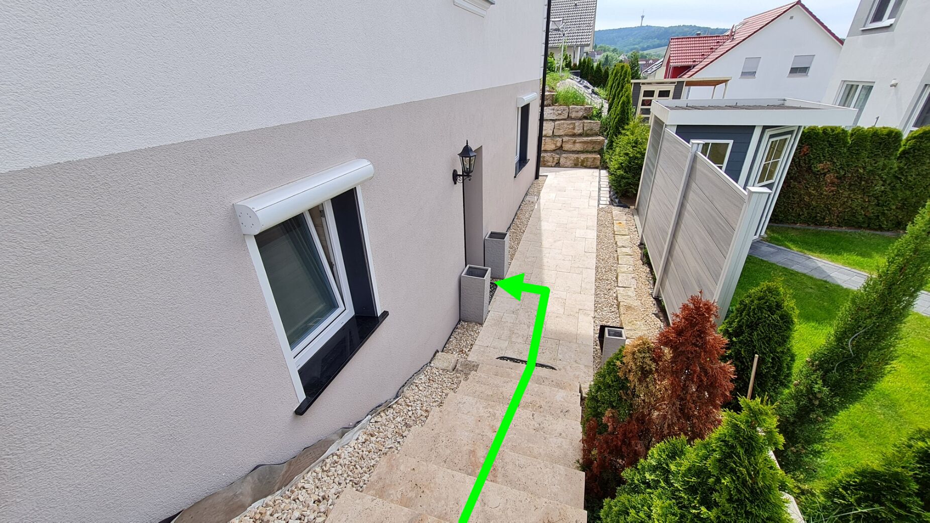 Un immeuble résidentiel avec une petite fenêtre, un chemin de pierre et une flèche verte indiquant une direction.