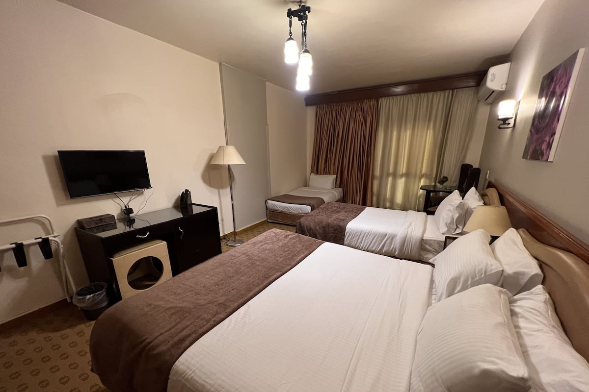 A hotel room with two beds, a desk, a television, and a washing machine.