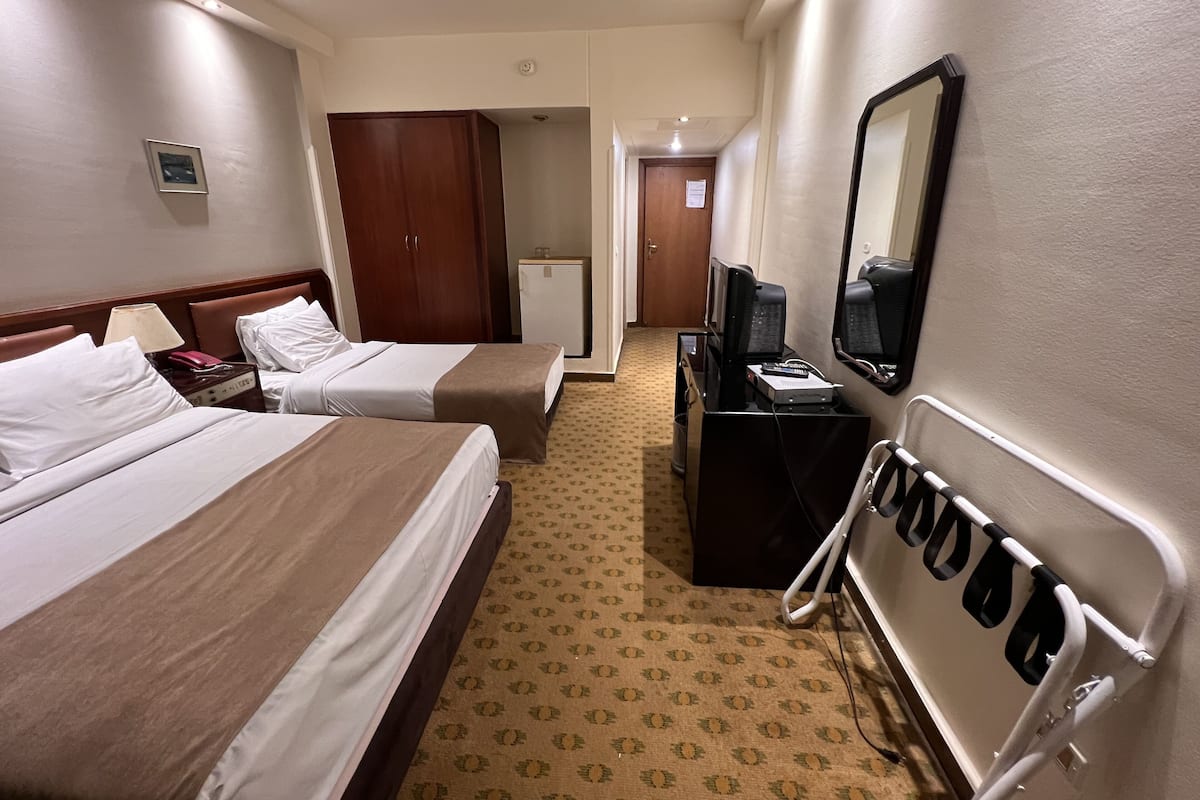 A hotel room with two beds, a desk with a computer, a mirror, and a minibar.