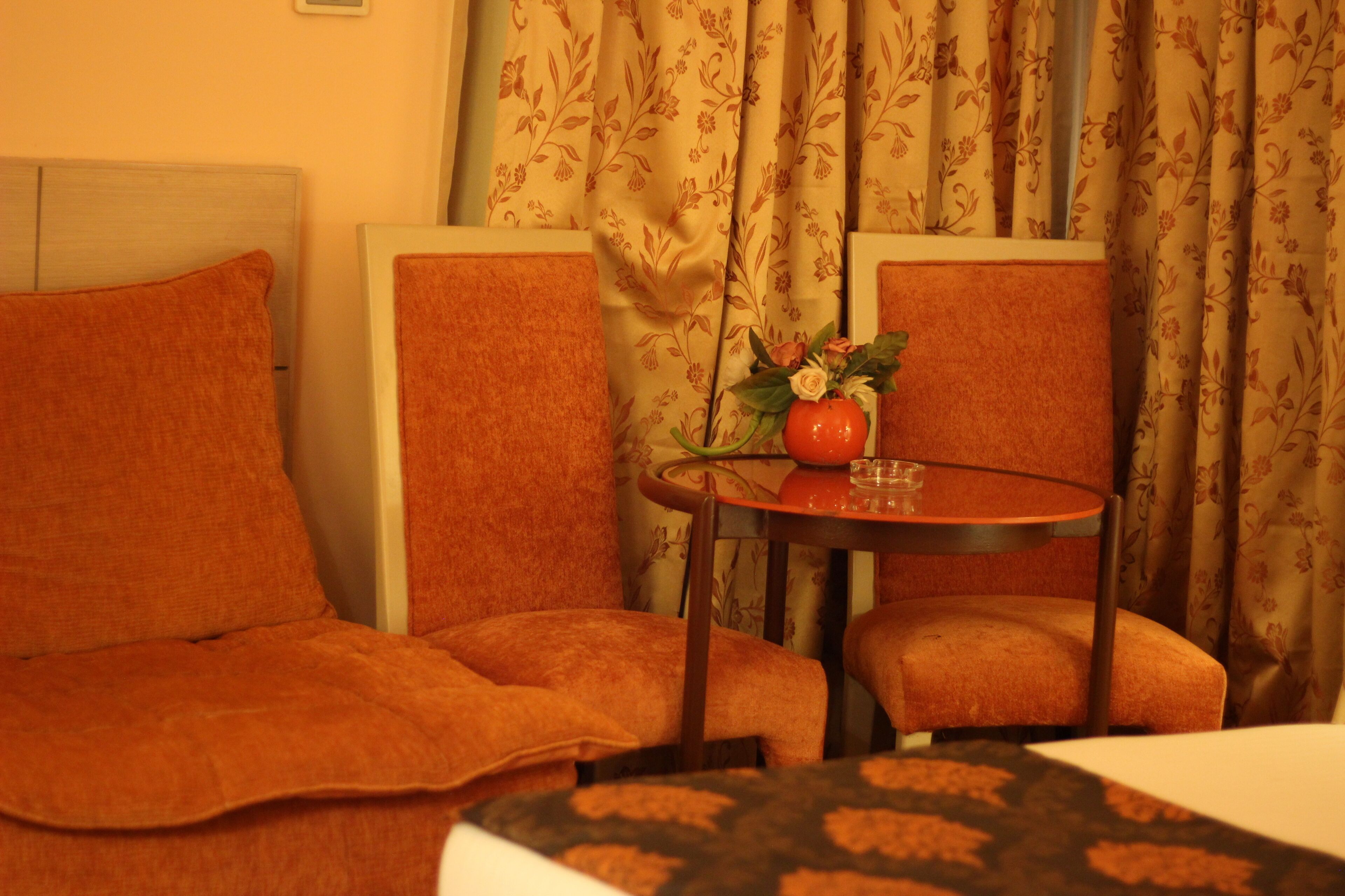 A hotel room with a bed, two armchairs, a small table with a vase of flowers, and curtains with a floral pattern.