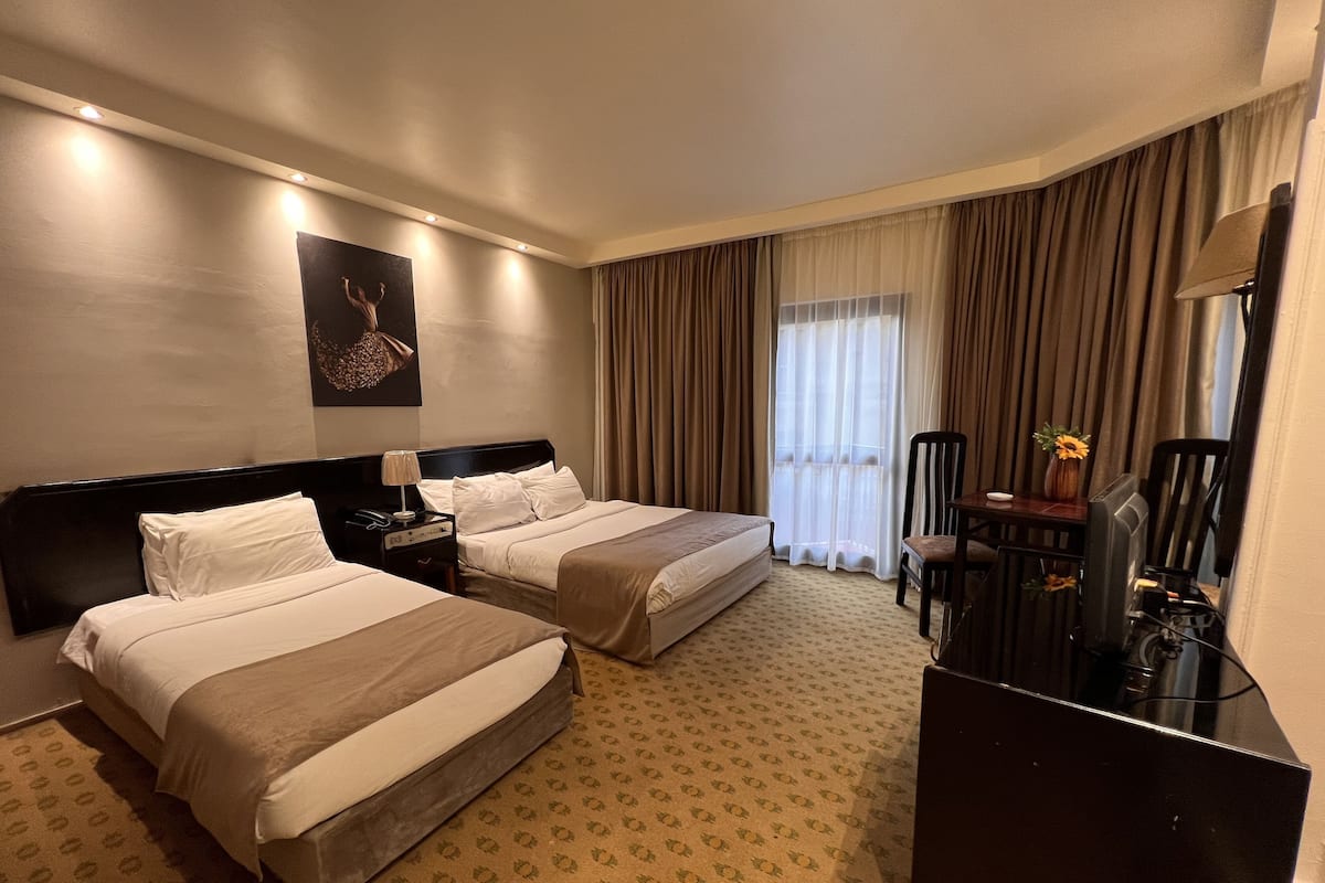A hotel room with two beds, a desk, a chair, a TV, and a window with curtains.