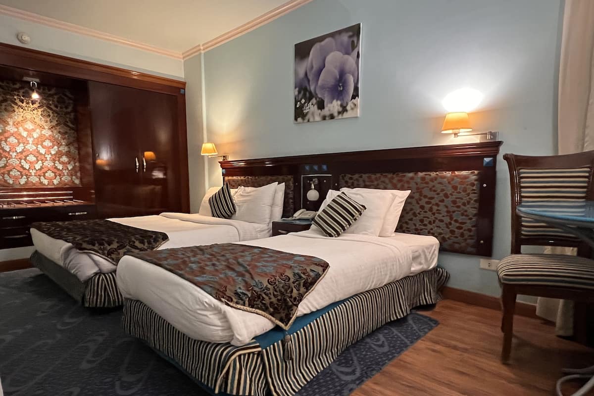 A hotel room with two beds, a wooden dresser, a chair, and a painting on the wall.