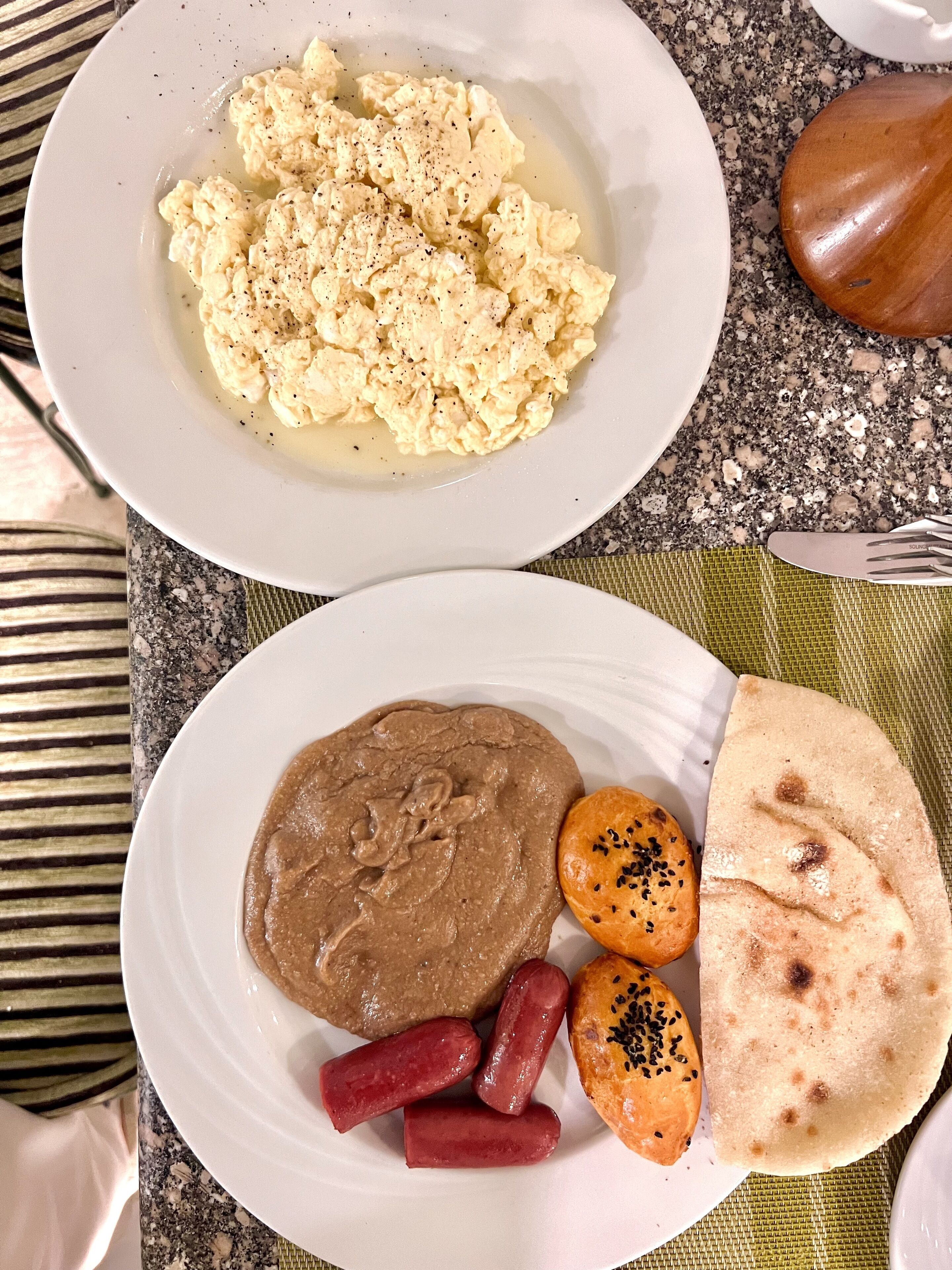 Two plates of food, one with scrambled eggs and the other with beans, sausages, and flatbread.