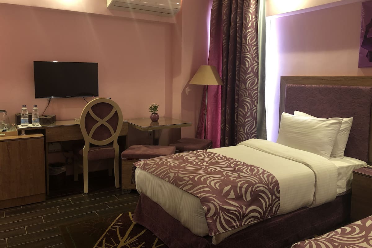 A hotel room with a bed, a desk, a chair, a TV, and an air conditioning unit.