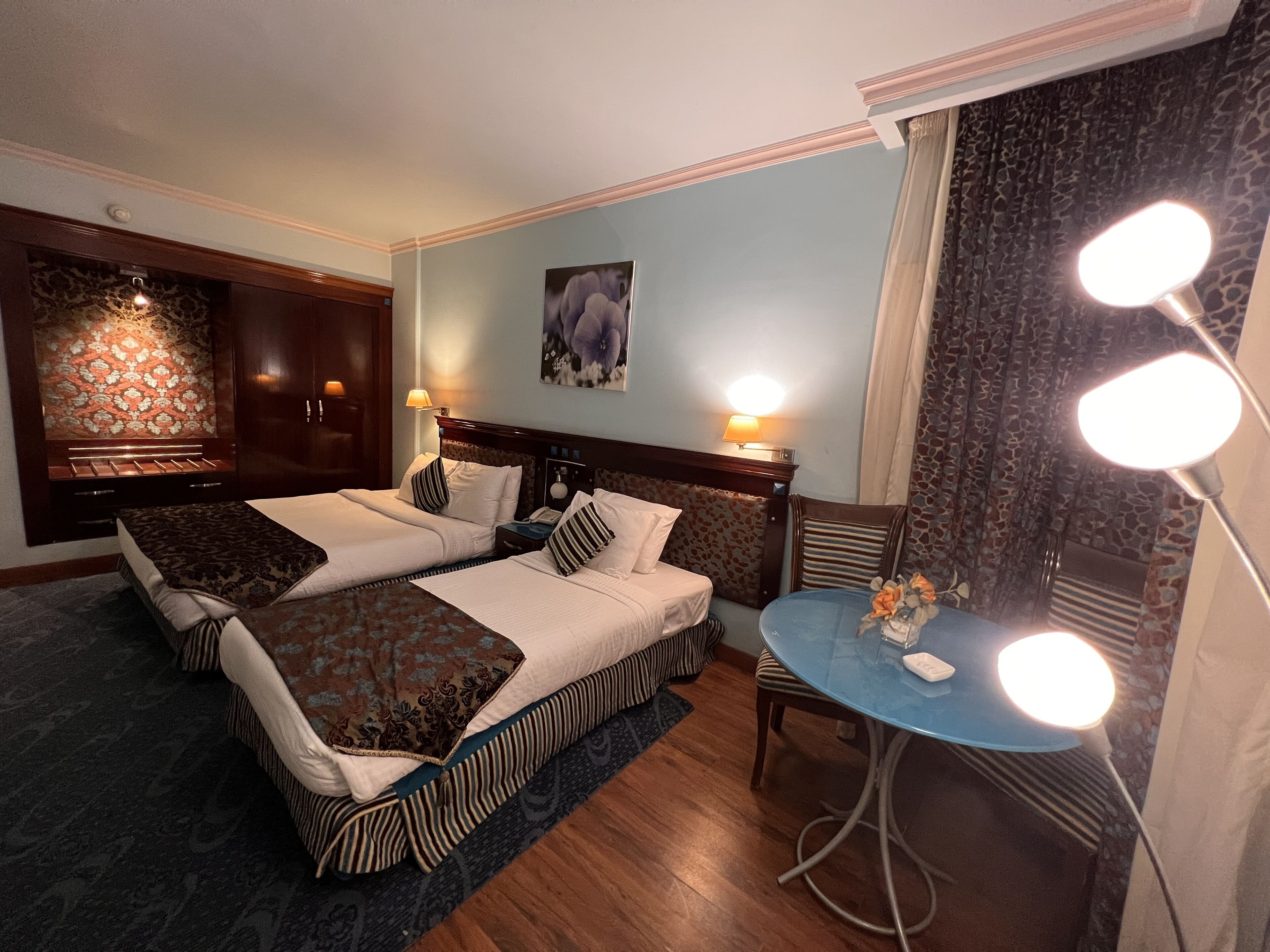 Une chambre d’hôtel avec deux lits, une petite table avec une lampe, un miroir et un panneau décoratif au mur.