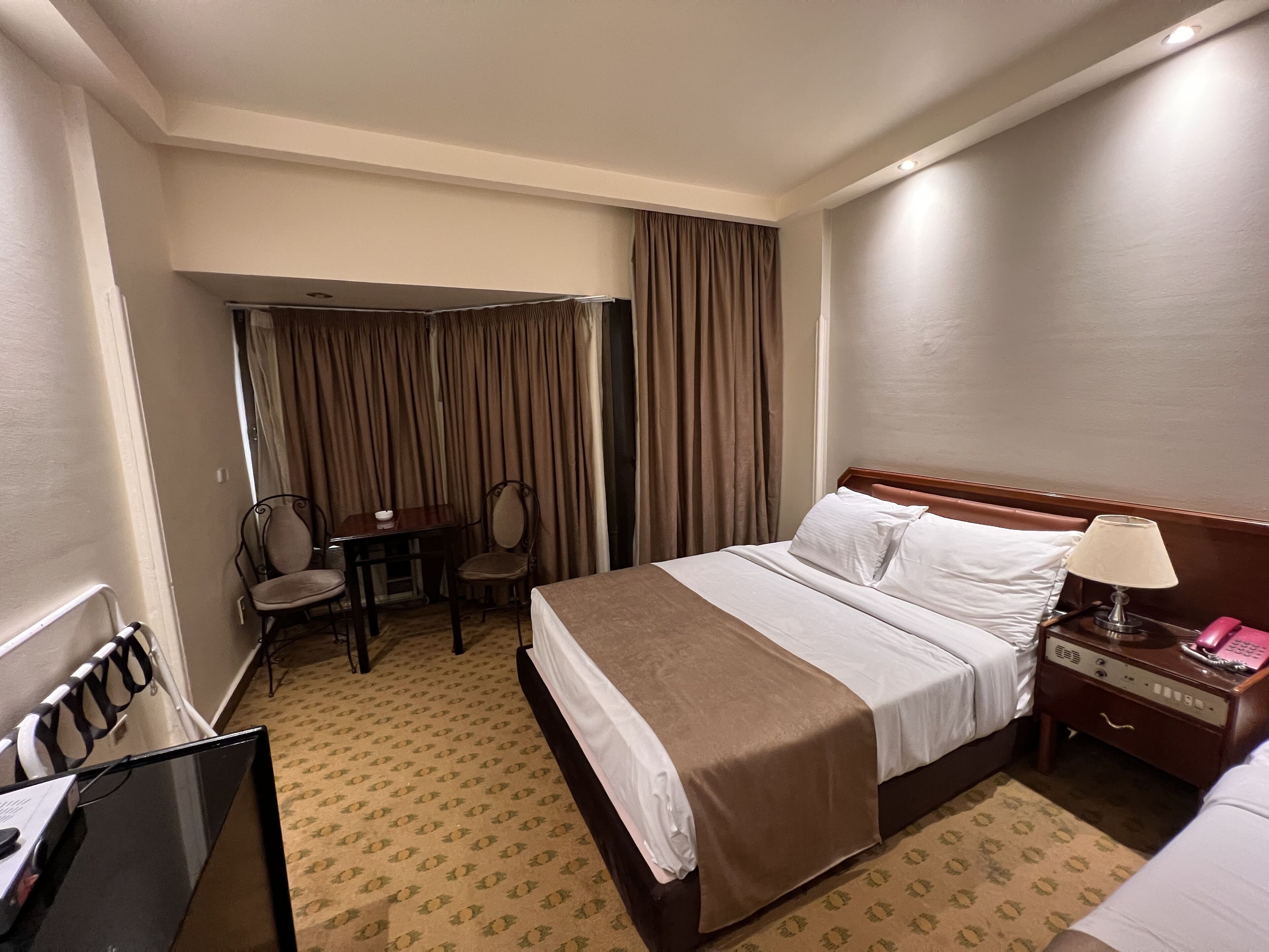 Una habitación de hotel con cama, escritorio, silla, mesita de noche y lámpara.