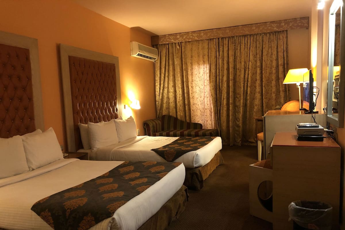 A hotel room with two beds, a sofa, a desk with a computer, and an air conditioning unit.