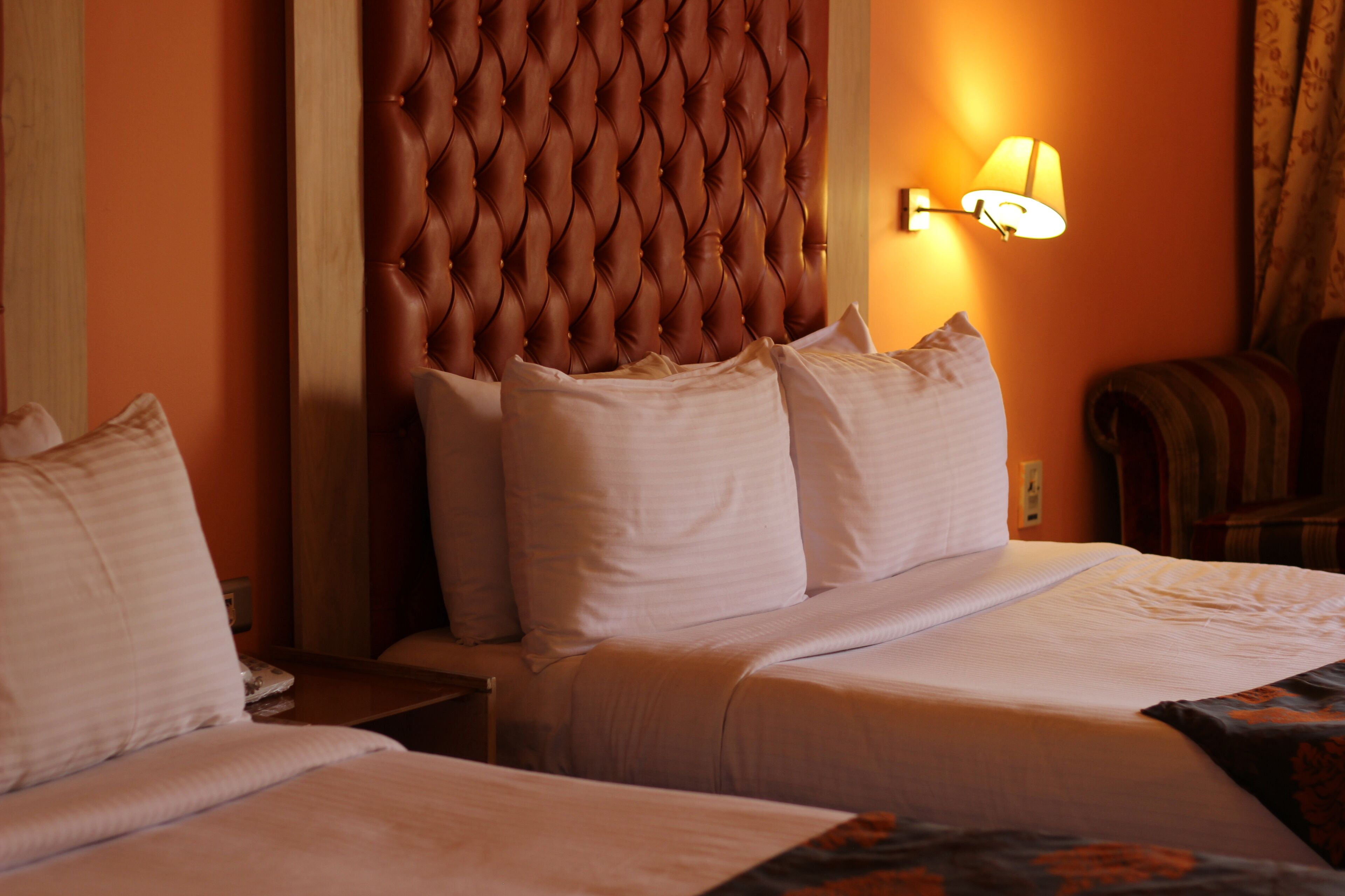 Habitación de hotel con un cabecero capitonado, una lámpara de noche y una cama bien hecha con ropa blanca.