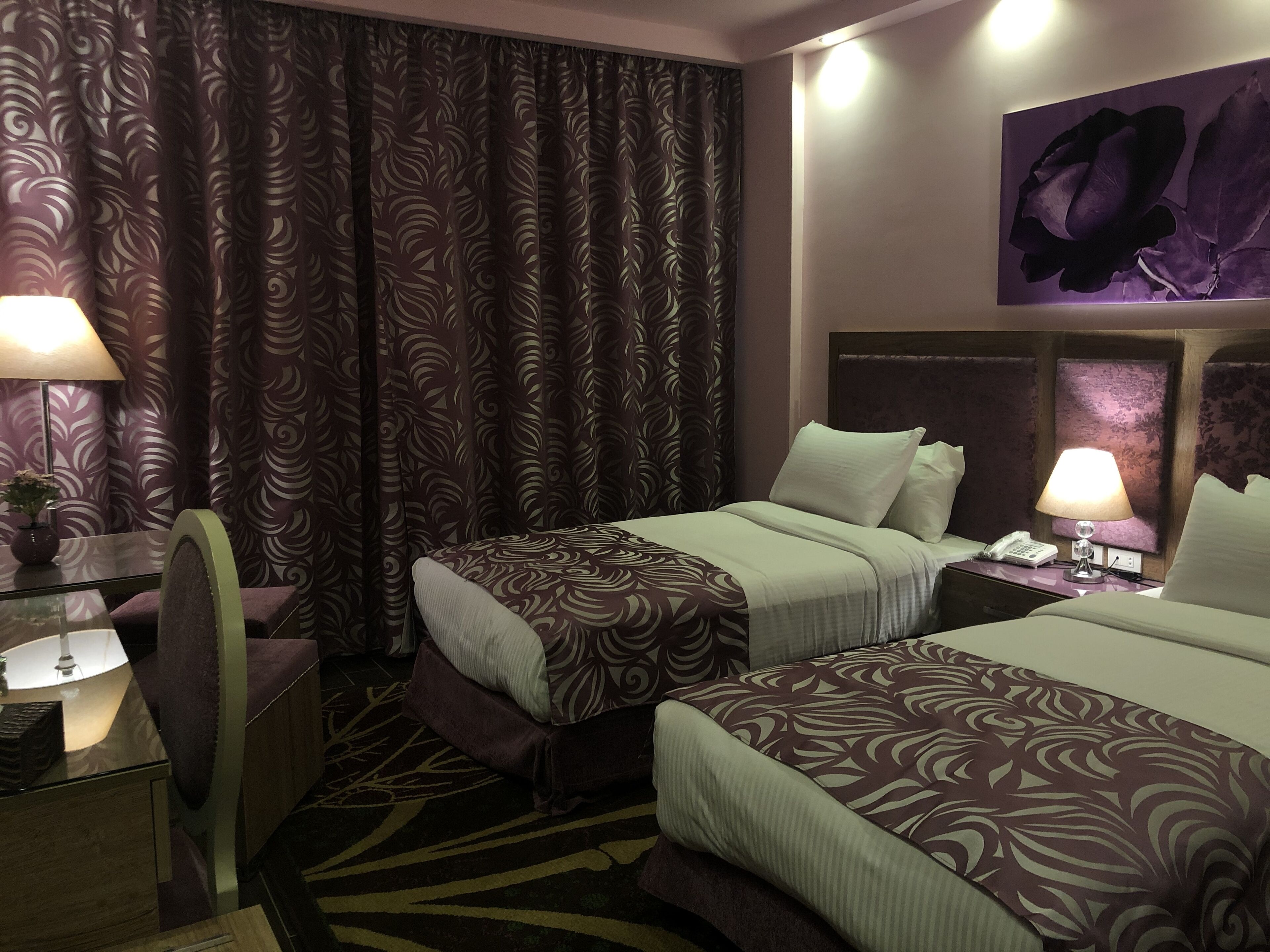 Habitación de hotel con dos camas, un escritorio, una silla, una lámpara y un cuadro en la pared.