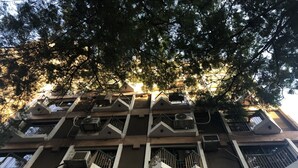 Um edifício com várias andares, varandas, aparelhos de ar condicionado e vista para árvores.
