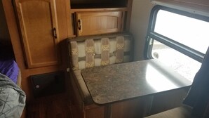 Un intérieur de camping-car compact comprenant un meuble en bois, un banc rembourré et une petite table.