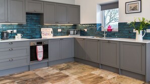 A modern kitchen with grey cabinets, a blue-tiled backsplash, a stainless steel sink, and a window with a view. - 2 bedroom accommodation in Llanfachraeth, near Holyhead (Llanfachraeth, near Holyhead)