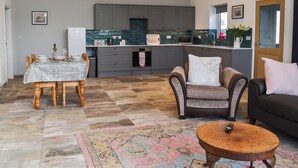 A spacious living area with a dining table, a sofa, a coffee table, and a kitchen in the background. - 2 bedroom accommodation in Llanfachraeth, near Holyhead (Llanfachraeth, near Holyhead)