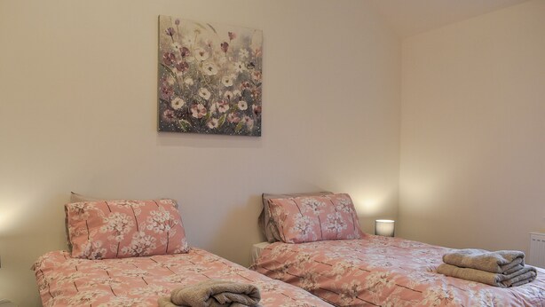 A room with two beds, each with floral bedding and pillows, a painting on the wall, and a lamp on the side table. - 2 bedroom accommodation in Llanfachraeth, near Holyhead (Llanfachraeth, near Holyhead)