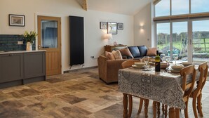 A spacious living area with a high ceiling, a dining table set for two, and a view through large windows. - 2 bedroom accommodation in Llanfachraeth, near Holyhead (Llanfachraeth, near Holyhead)