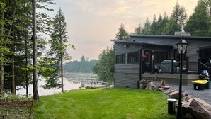 Una cabaña junto al lago con un porche, un jardín césped y vistas al lago.