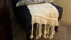 Una sedia con una fodera scura e una coperta lavorata a maglia bianca.