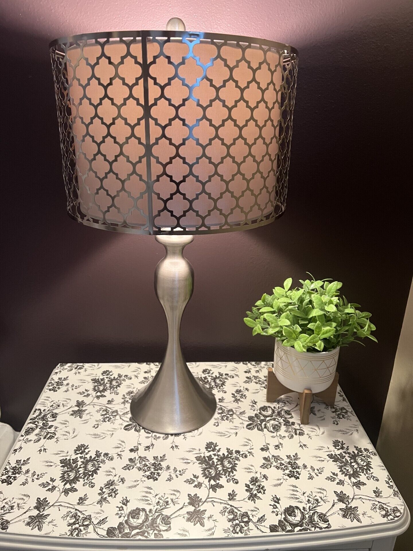 Une lampe de table avec un abat-jour à motifs, une plante en pot et une nappe à fleurs.