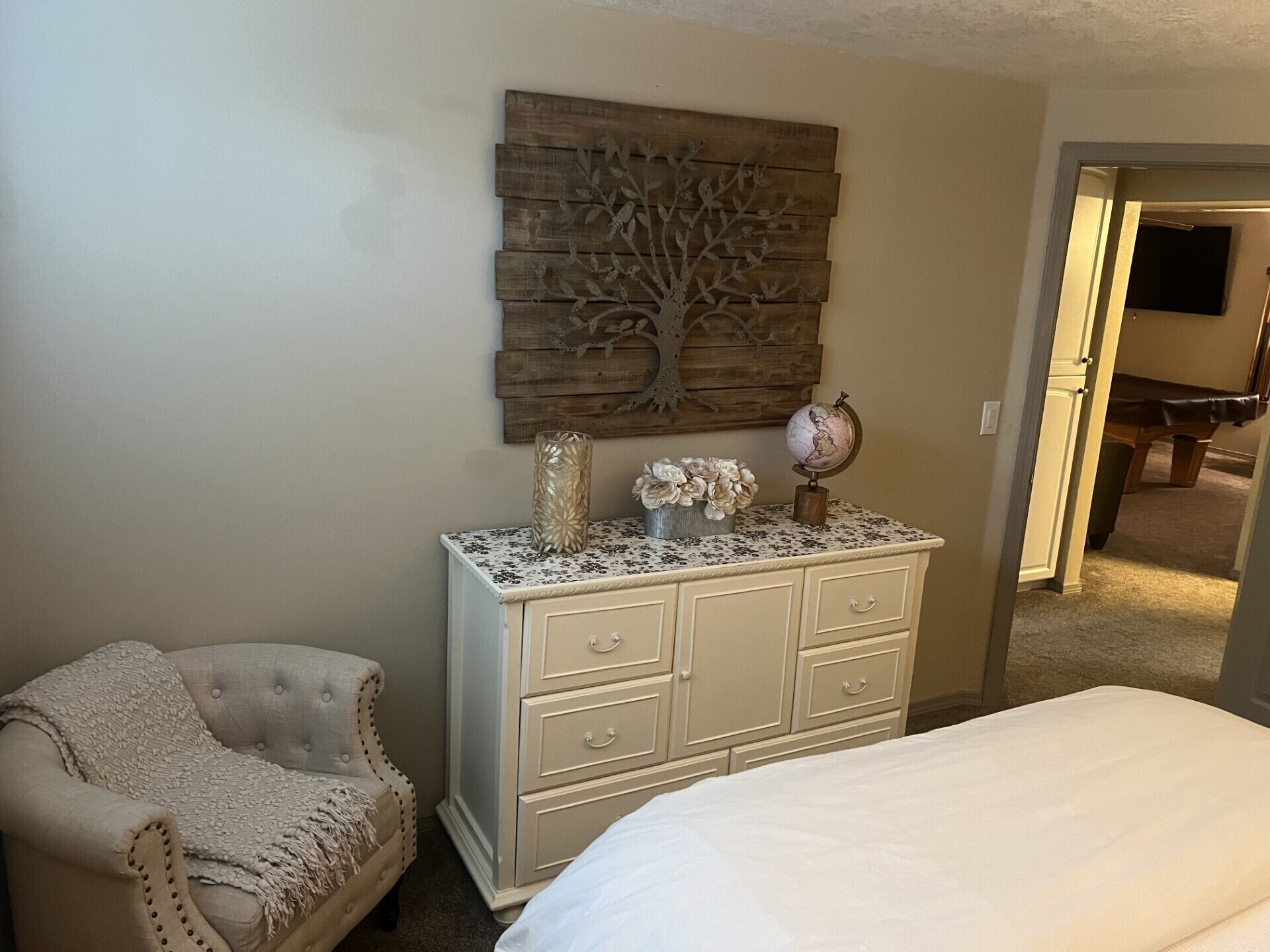 A bedroom with a bed, a dresser, a chair, and a wall-mounted decorative piece.