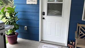 Et blå hus med en hvid dør, dørmåtte, en potteplante og et skilt med teksten "To the Hostess Kiosk".