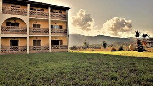 A multi-story building with balconies, a grassy lawn, and mountains in the background. - Elpida Hotel (Zakynthos)