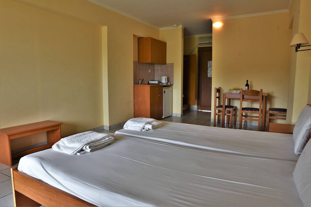 A hotel room with two beds, a kitchenette, and a dining area.