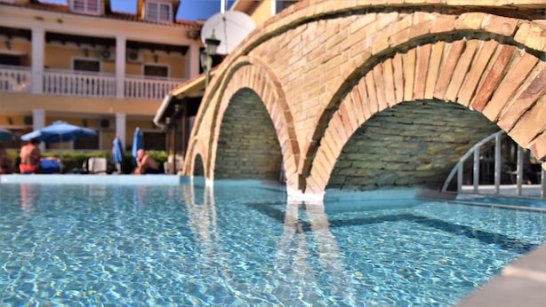 A clear pool with a stone bridge in the background. - Elpida Hotel (Zakynthos)