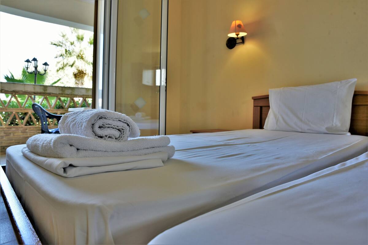 A hotel room with a bed, a wall-mounted lamp, and a view of the outdoors.