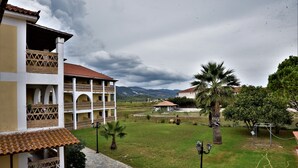 A courtyard with a building featuring a tiled roof, a stone pathway, and a palm tree. - Elpida Hotel (Zakynthos)