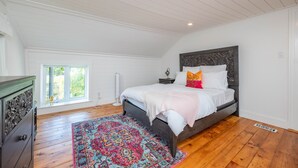 Un dormitorio con una cama grande, un aparador de madera, una alfombra colorida y una ventana con vistas al verdor.