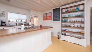 Una cocina moderna con armarios blancos, encimera de granito y una unidad estantería empotrada que exhibe diferentes platos y cristalería.
