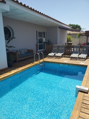 Ein Schwimmbecken mit Holzterrasse, Liegestühlen und einer Sitzecke.