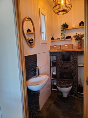 Ein Badezimmer mit einem weißen Waschbecken, einer Toilette, einem Spiegel und einer Pendelleuchte.