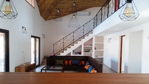 Una sala de estar moderna con techo de madera, una escalera y un área de descanso con cojines coloridos.