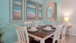 Un comedor con una mesa de madera dispuesta para seis personas, sillas blancas y vista al océano a través de una ventana.