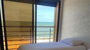 A room with two beds, a view of the beach, and a sliding glass door leading to the balcony.