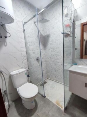 Une salle de bain comprenant des toilettes, une douche fermée par une paroi de verre et un lavabo.