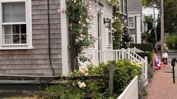 A residential house with a white picket fence, a garden with pink flowers, and a brick pathway.