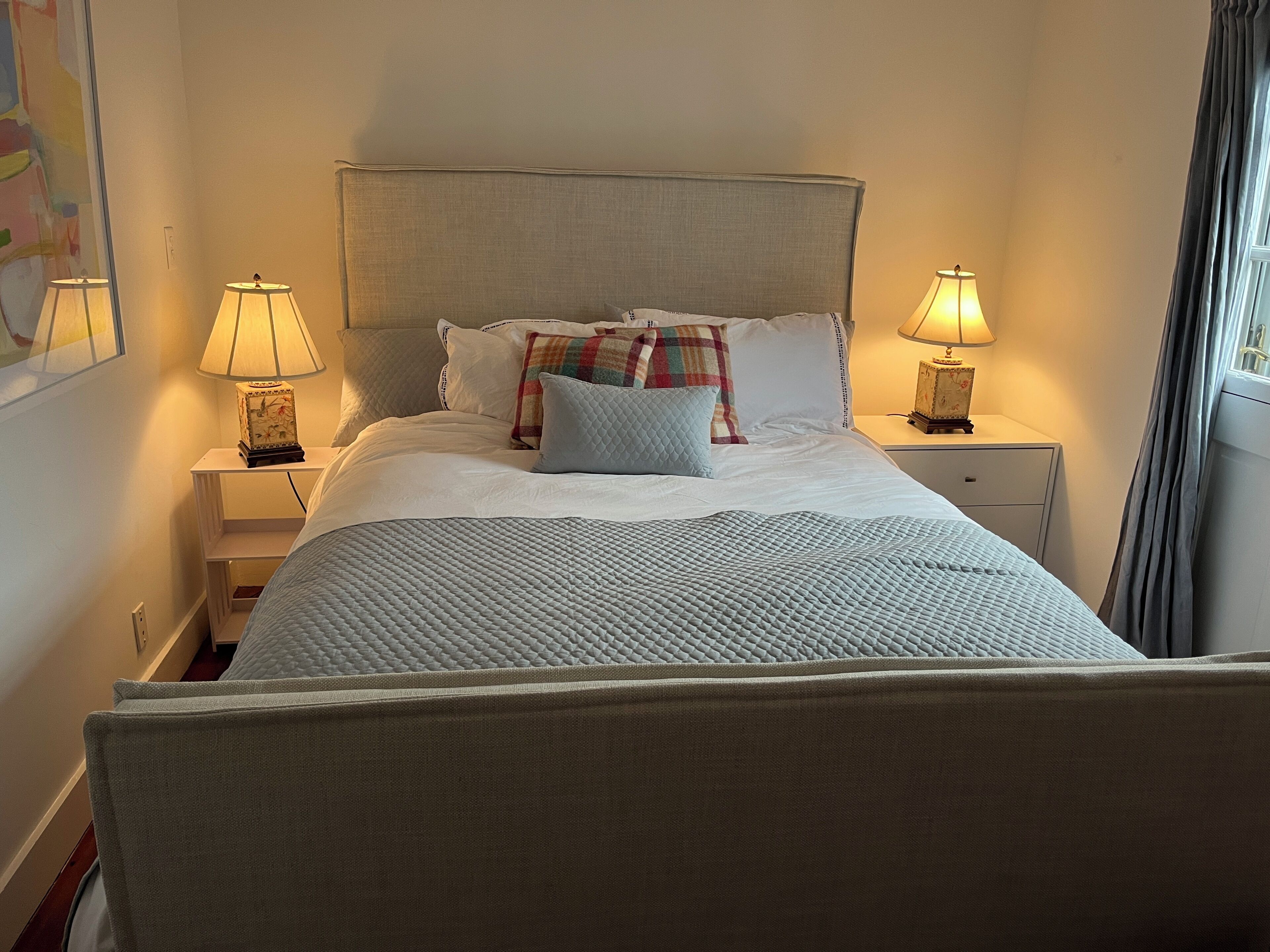 A neatly made bed with a quilted blanket, two bedside lamps, and a nightstand with a lamp.