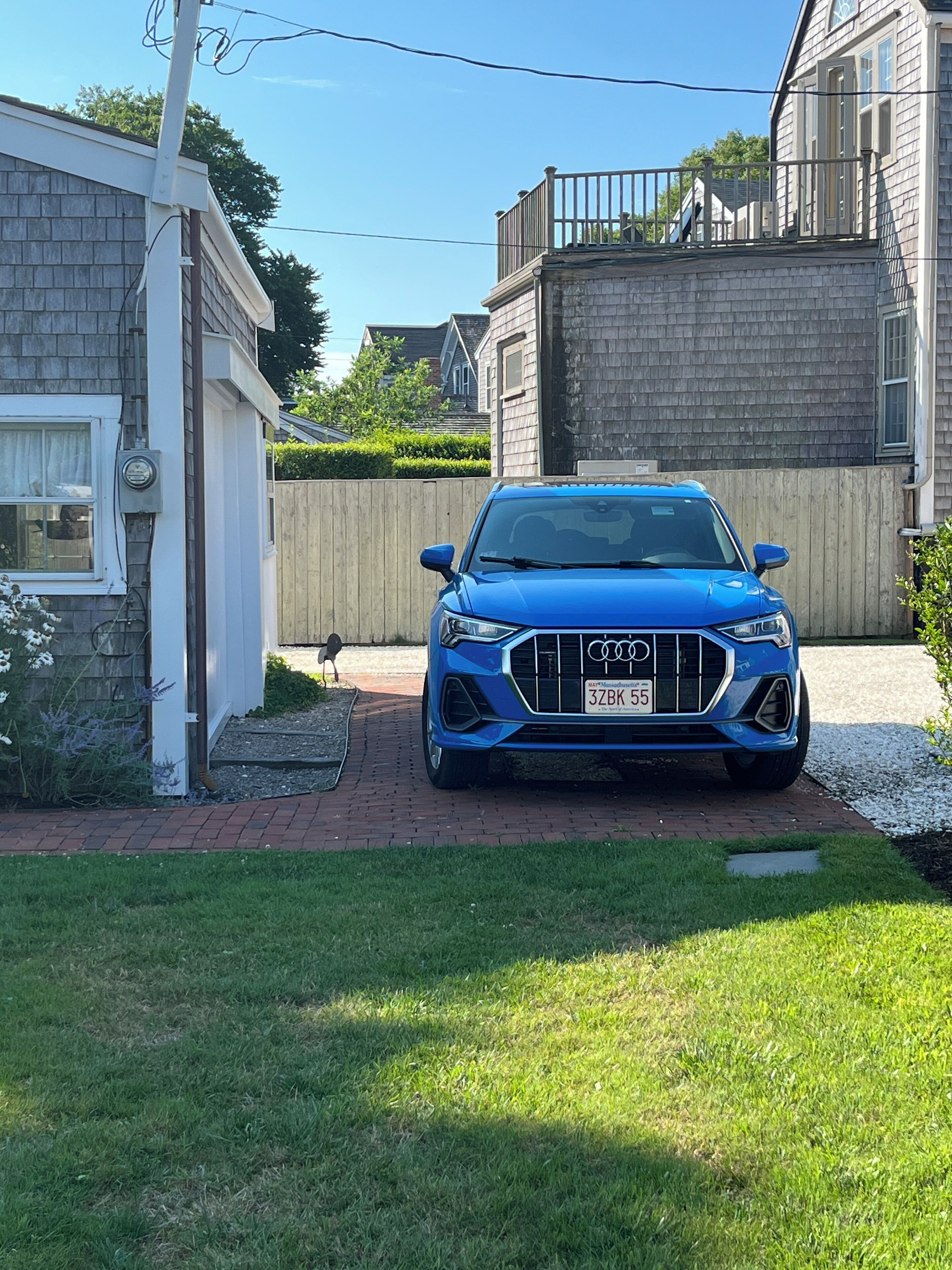 Ein blauer Audi steht auf einer Auffahrt mit einem Ziegelweg, der zu einem Haus führt.